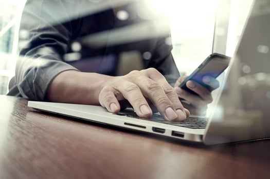 A man working with his laptop and smartphone in the frame